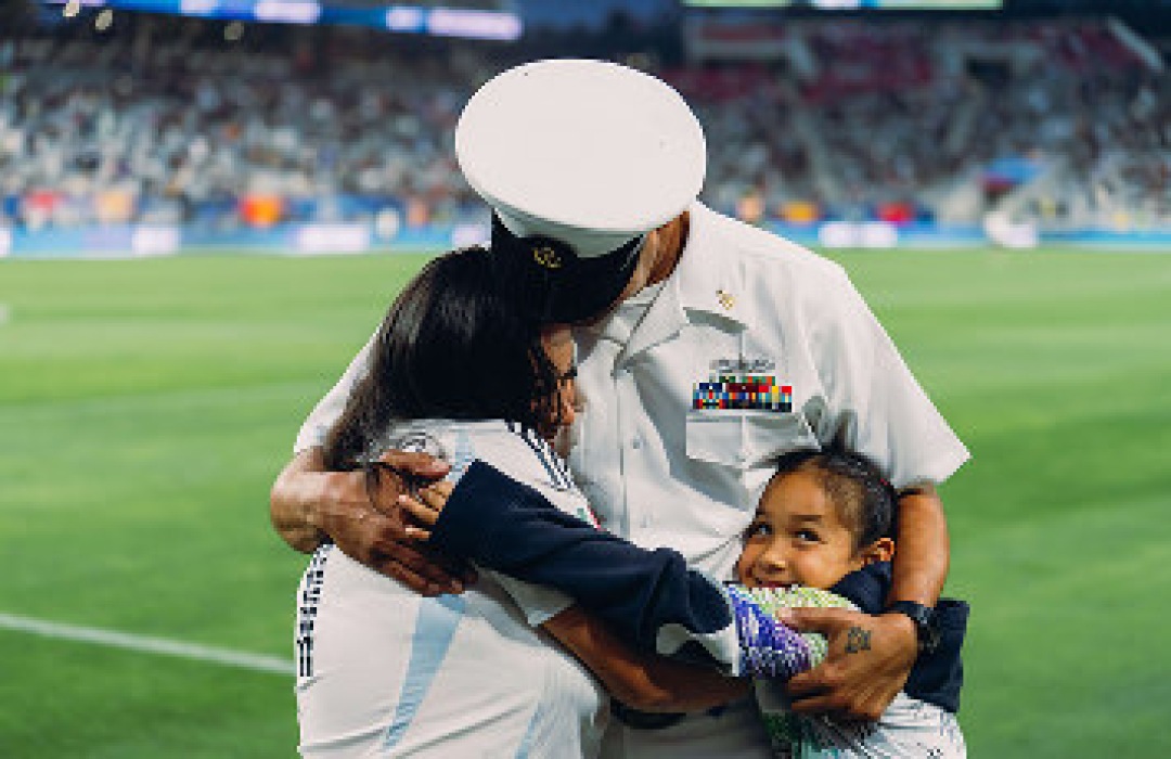 Military service member hugging his family on a stadium field.