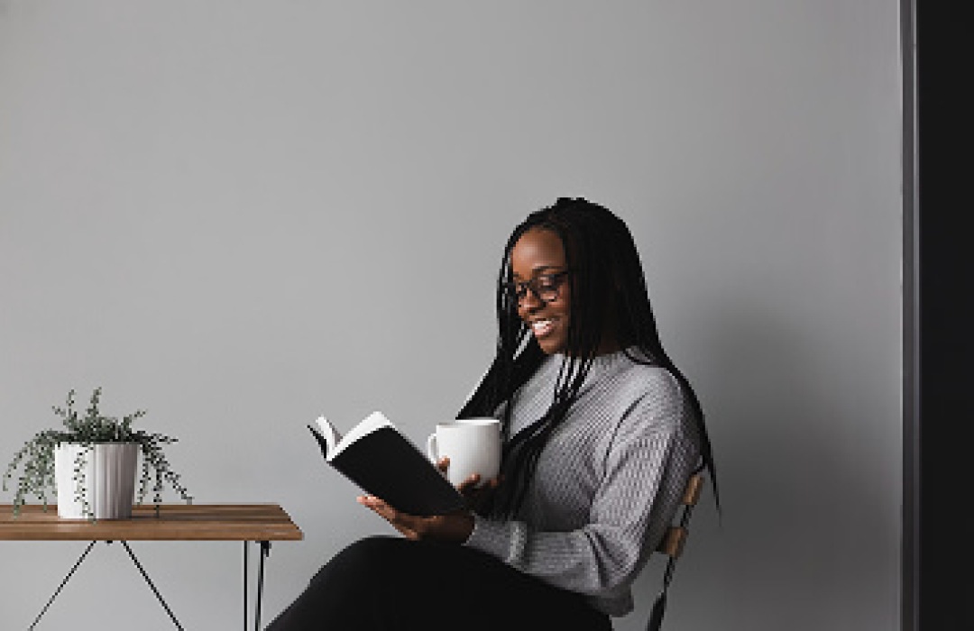 Woman smiling while reading a book and holding a mug.
