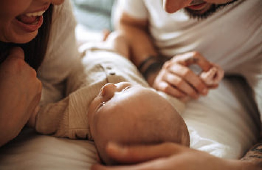 Parents leaning over their newborn baby on a bed.