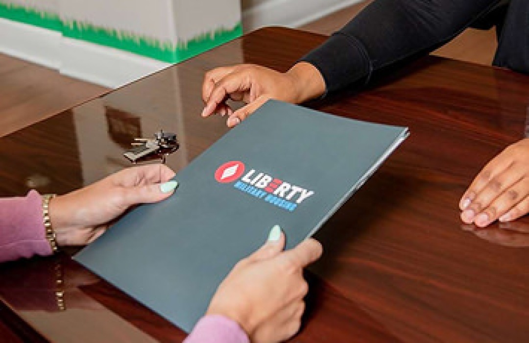 Handing over a Liberty Military Housing folder across a desk.