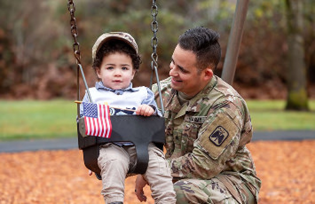 Military father playing with his toddler on a playground swing.
