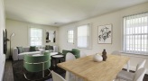 large room with dining room table and white chairs, green padded chair facing couach, three windows in room, art on wall