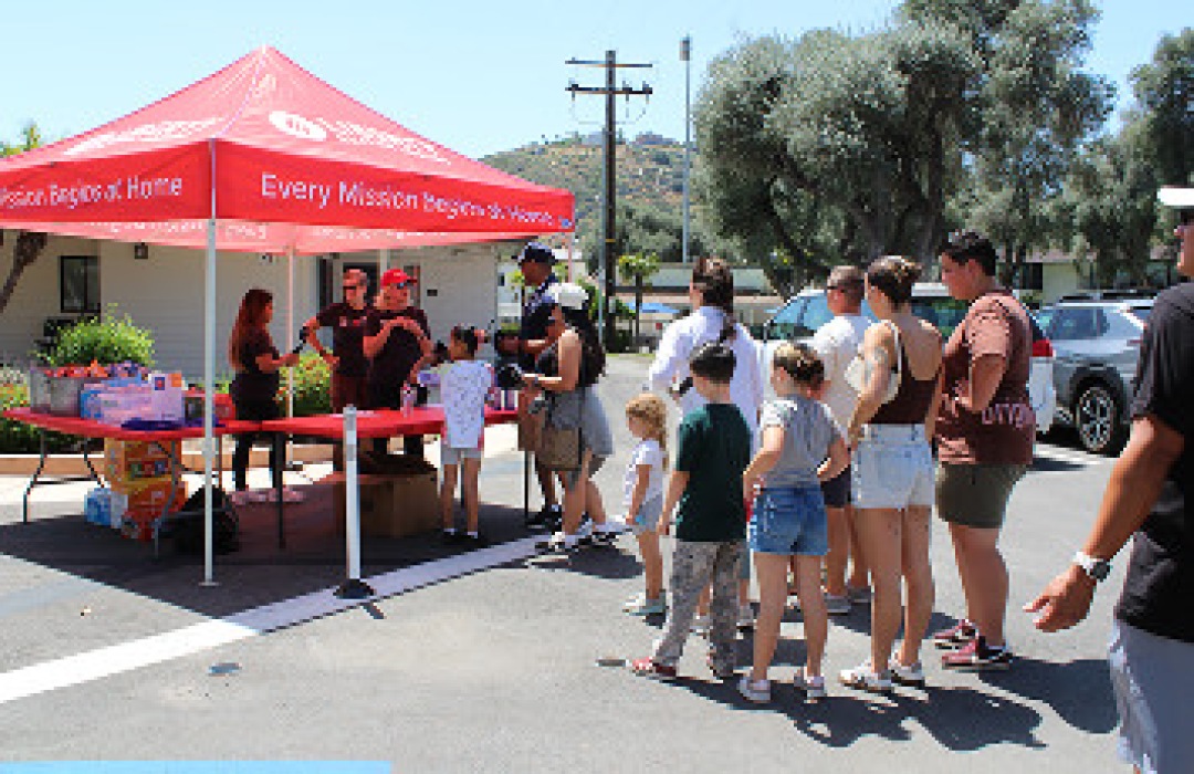 People lined up at an outdoor community event tent.