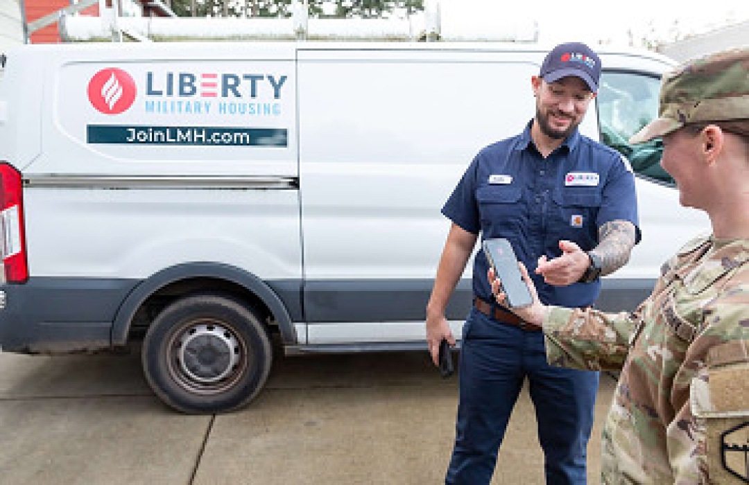 Service technician showing a smartphone screen to a military member next to a work van.