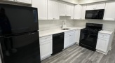 kitchen with black appliances, white countertop and cabinets, and gray flooring