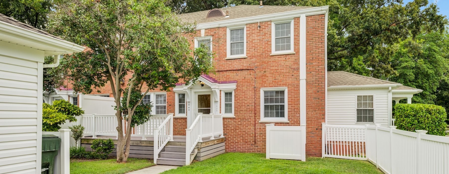 a brick house with a white fence and front yard