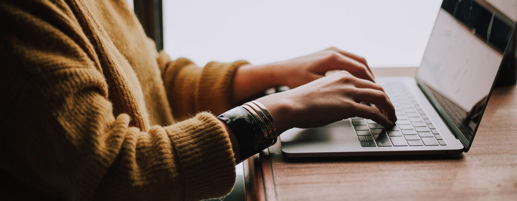 woman types on her laptop near large window