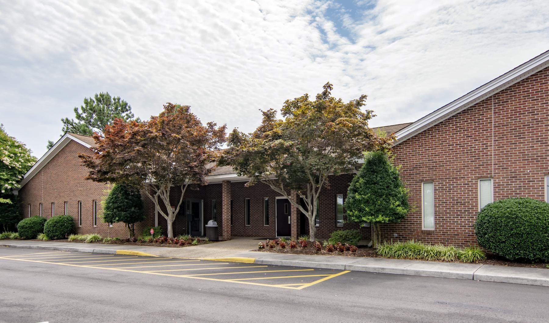 a brick building with trees and a parking lot