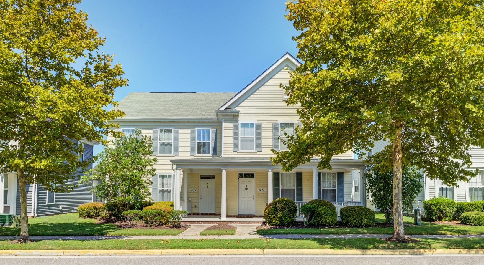 exterior of yellow house with two trees on each side