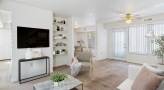 living room with tv mounted on wall, with sofa table under it.  Couch with pillow, chair with blanket, around TV.  bookshelf with nicknacks 