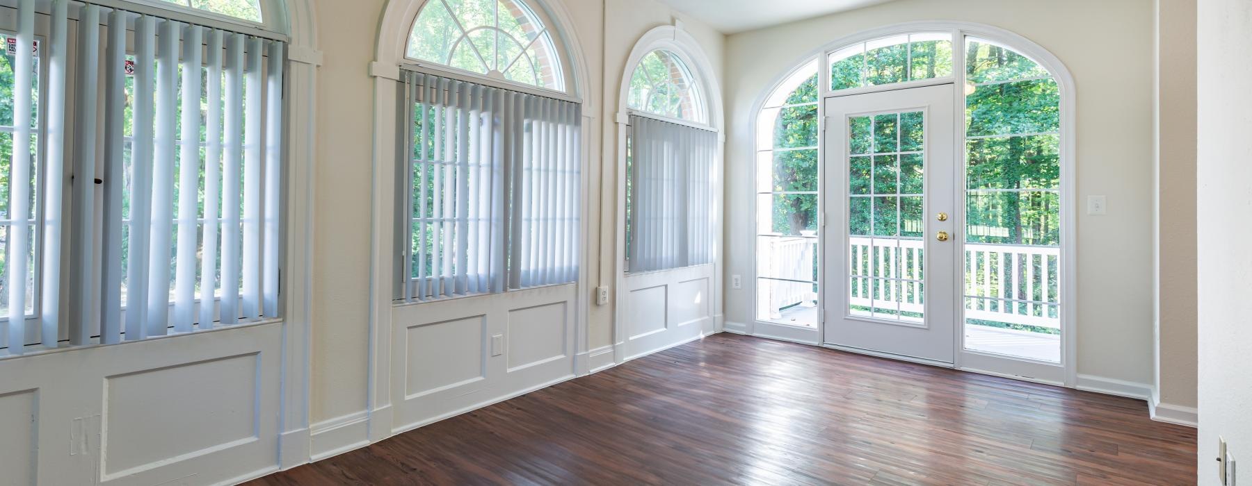 a room with a wood floor and windows with a ceiling fan