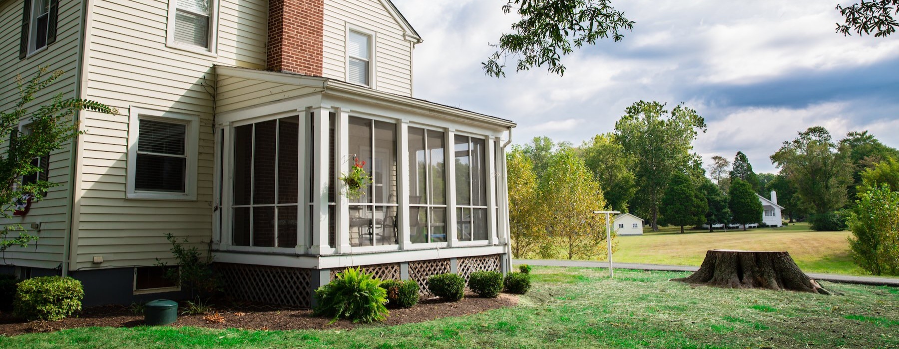 a white home with grass and a tree stump in front of it