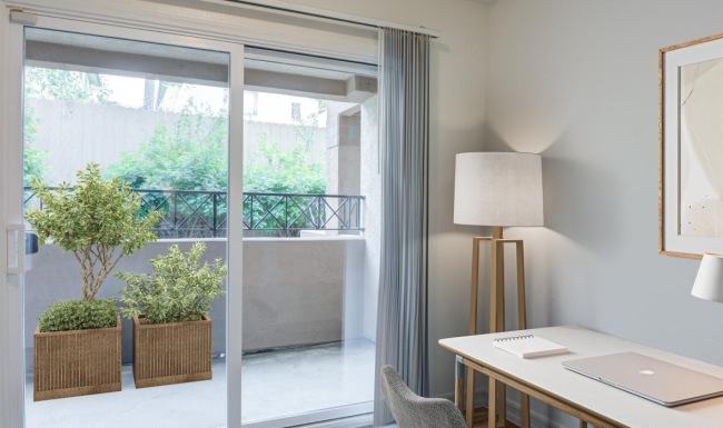 a room with a desk and a window with plants