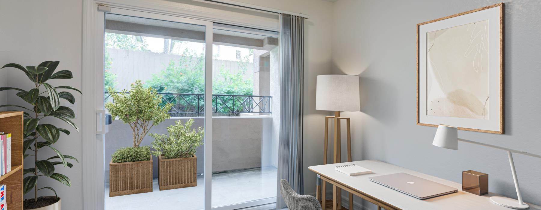 a room with a desk and a window with plants