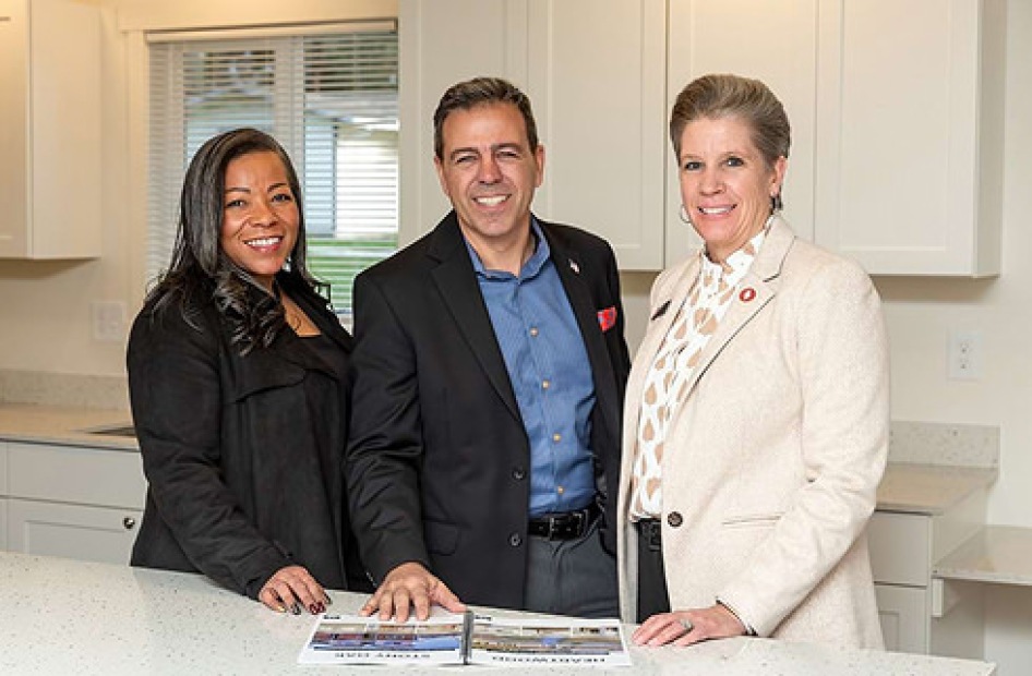 Three business professionals standing together in a kitchen.