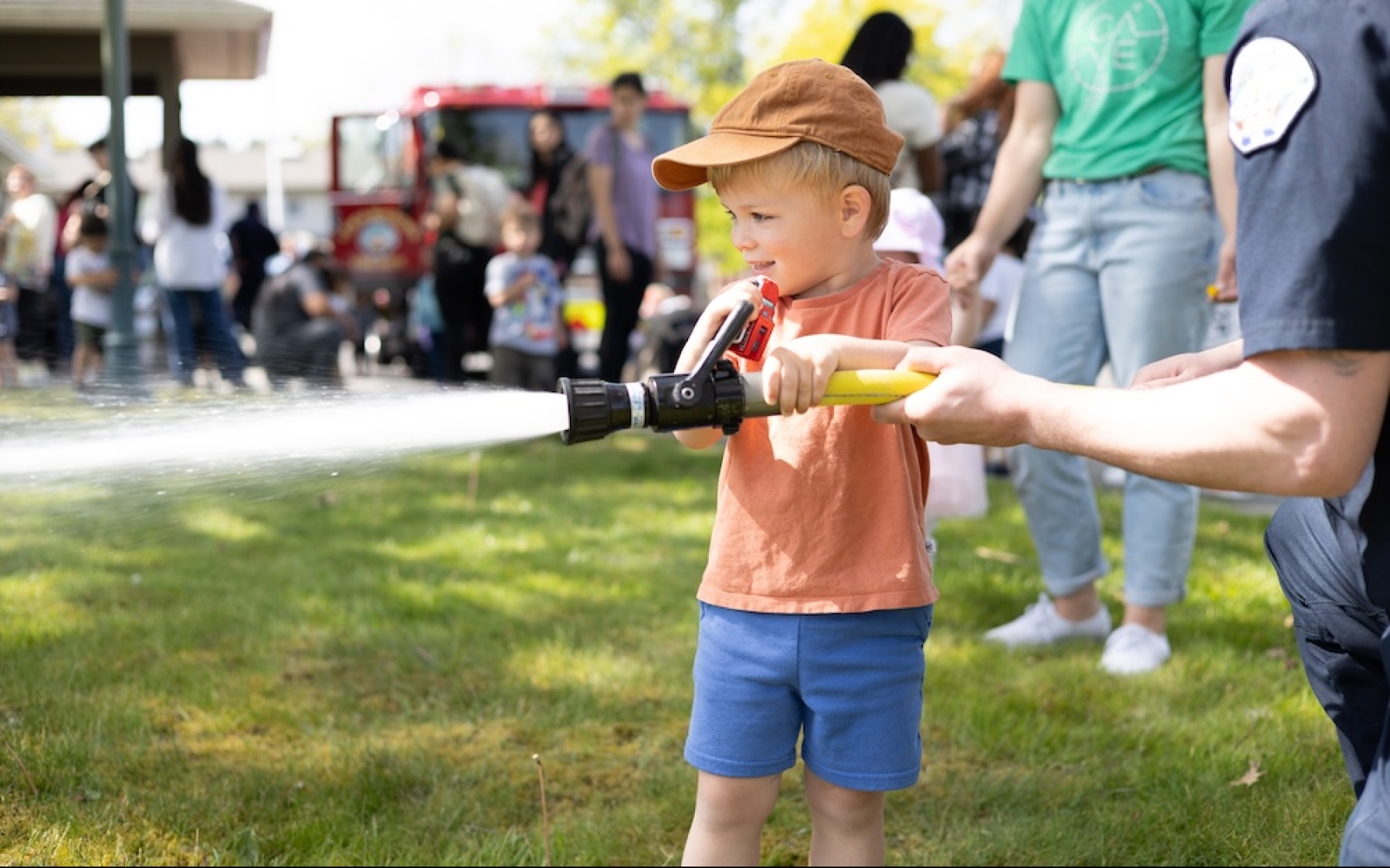 a boy holding a fire hose with a fire fighter