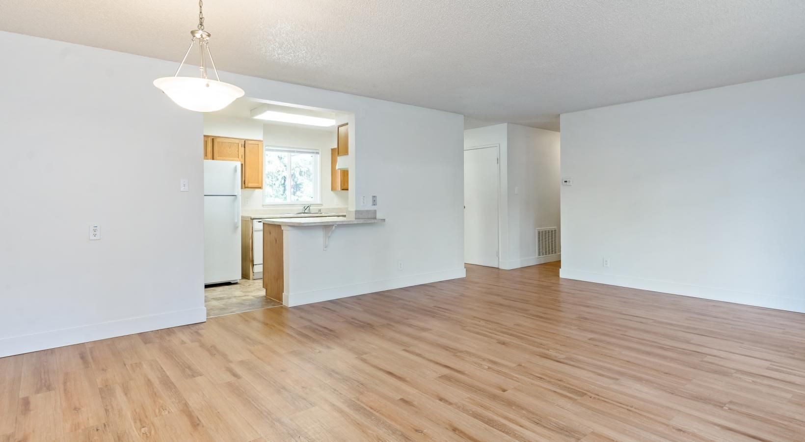 a large empty room with a chandelier and wood-style floors