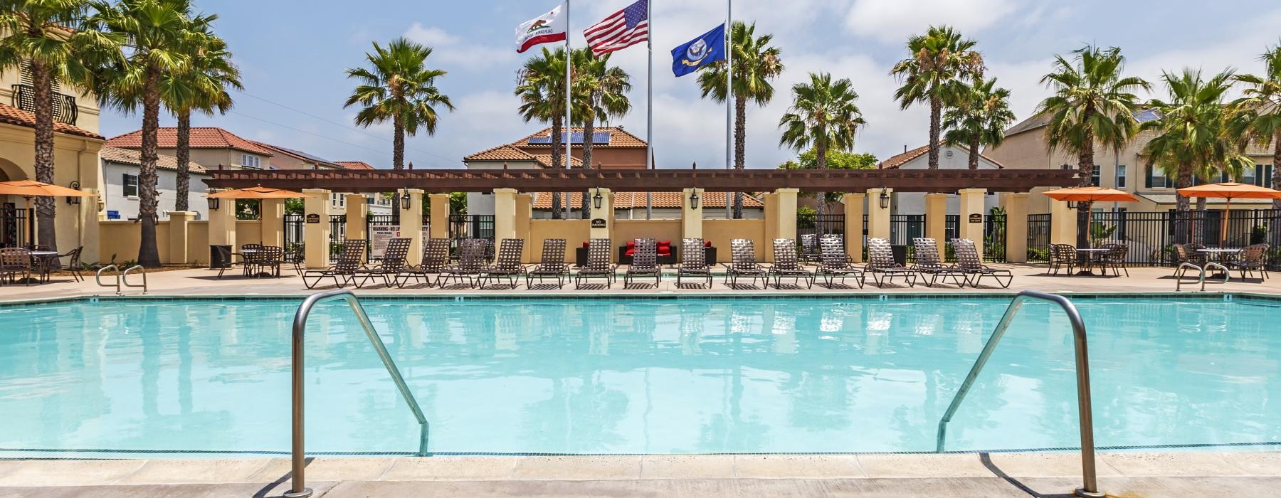 a pool with chairs and umbrellas by a building with flags